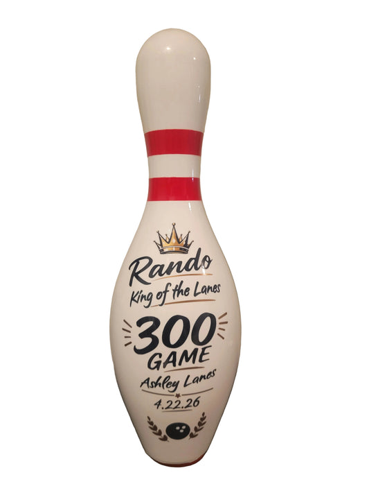A custom bowling pin with red stripes and black text reading 'Rando King of the Lanes 300 GAME Ashley Lanes 4.22.